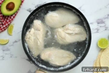 Chicken breasts are poached in water in a small saucepan.