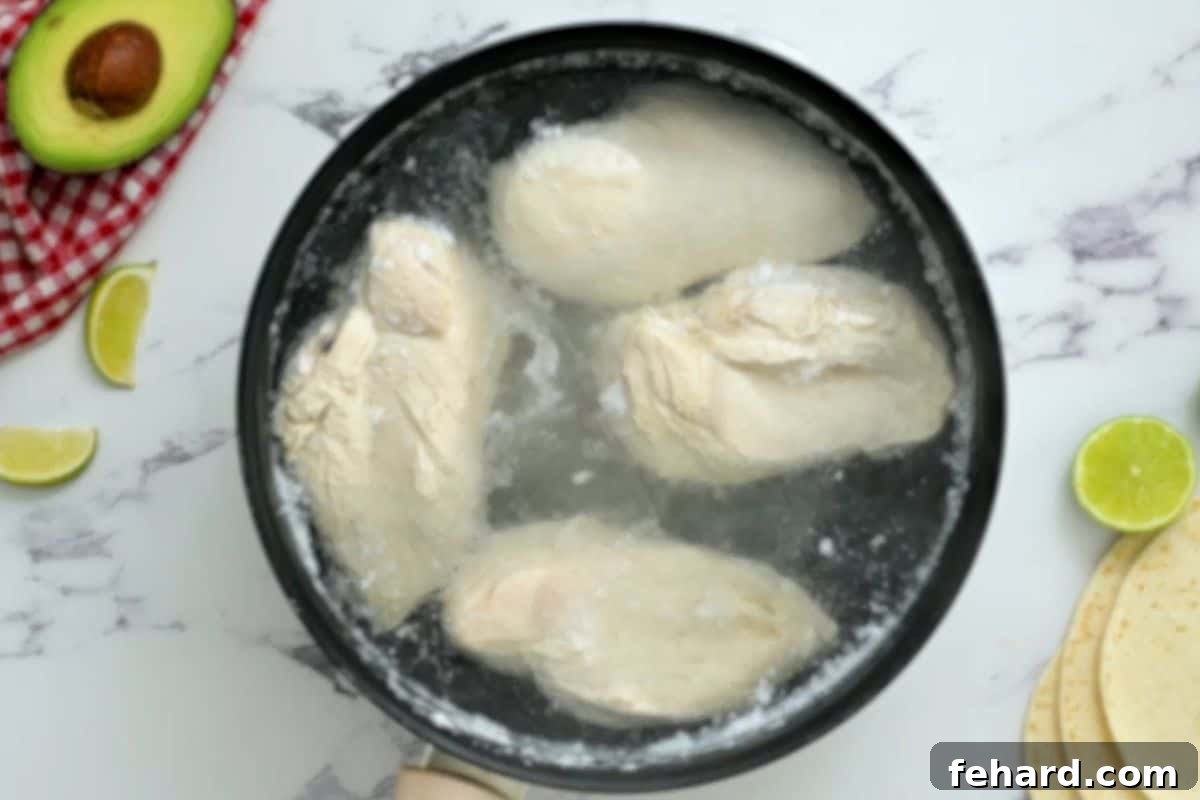 Raw chicken breasts gently poaching in salted water in a medium-sized saucepan on the stovetop.
