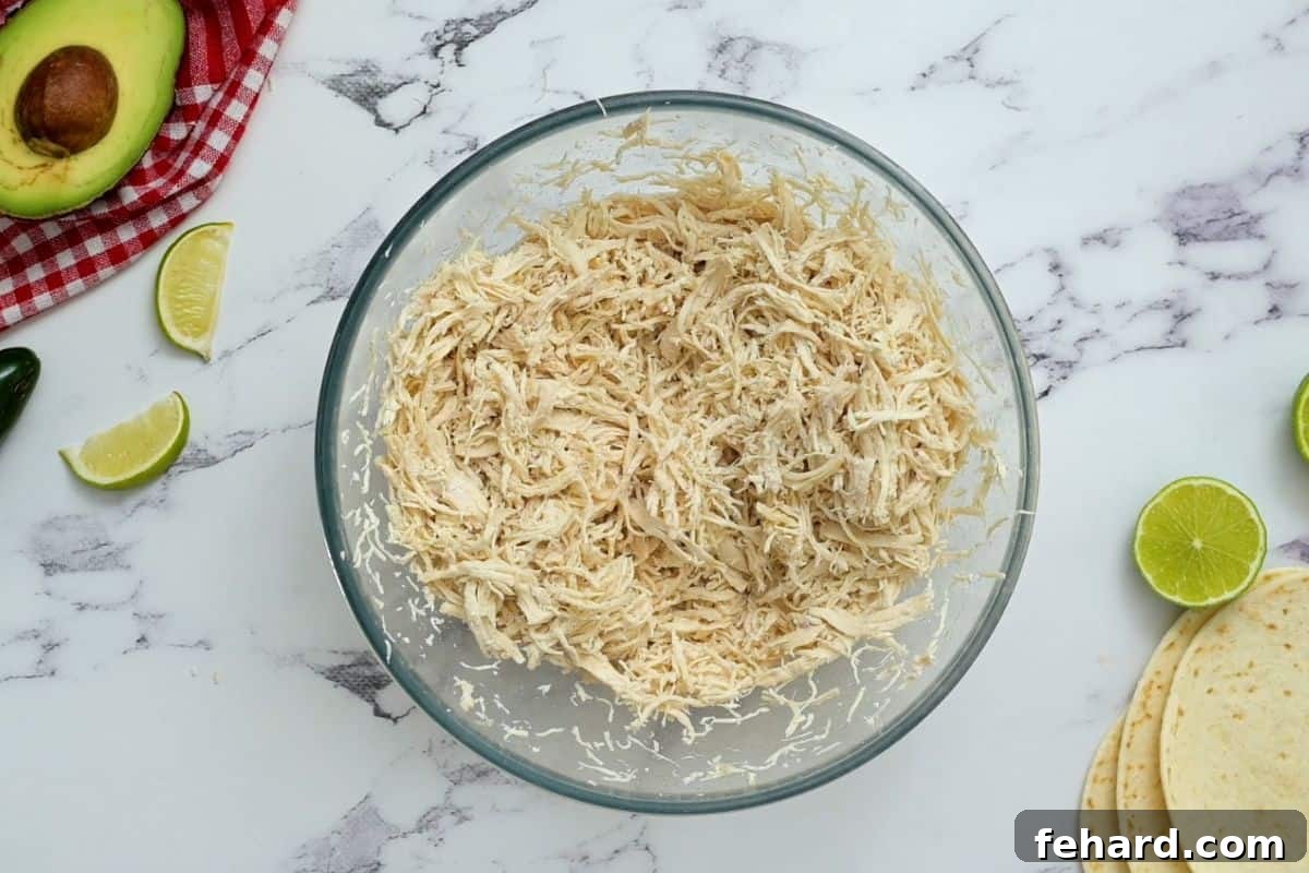 A large mixing bowl filled with freshly shredded, tender chicken, ready for seasoning.