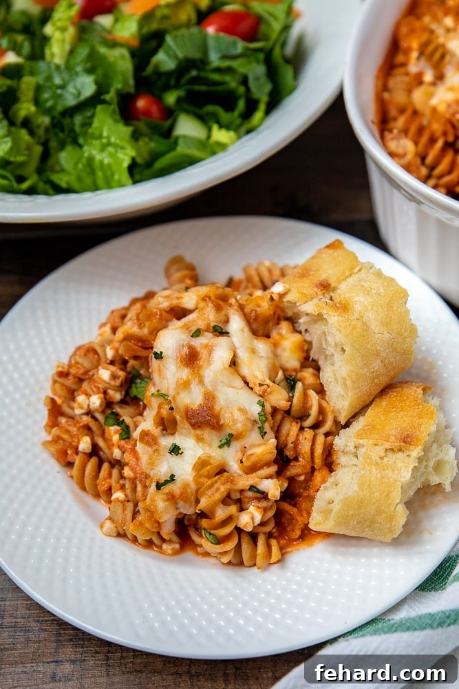 Serving of cheesy rotini pasta bake on white plate with a fork, ready to eat