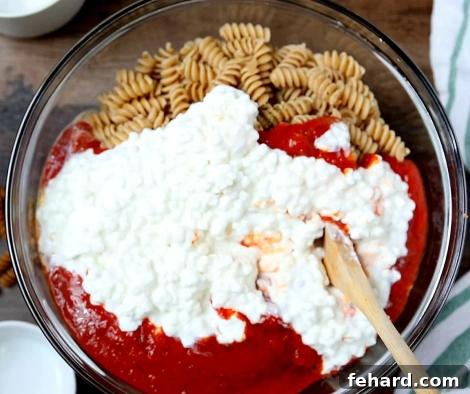 Clear Mixing Bowl with cooked rotini, spaghetti sauce, and cottage cheese, ready to be combined for the pasta bake.