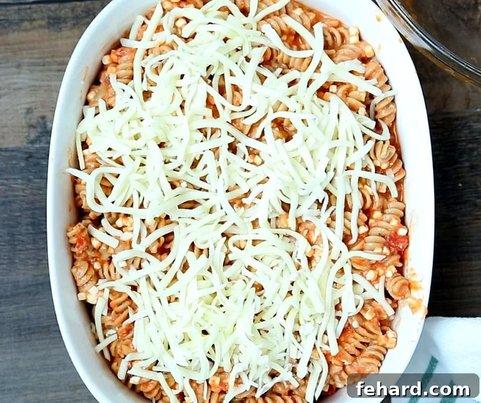 Rotini Pasta mixture in a clear baking dish, topped with shredded mozzarella cheese, before baking.
