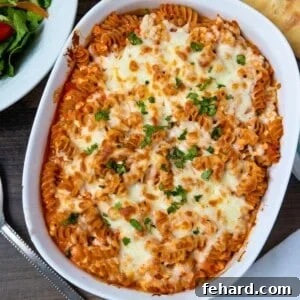 Cheesy Italian Baked Rotini in white casserole dish topped with fresh minced parsley next to tossed salad.