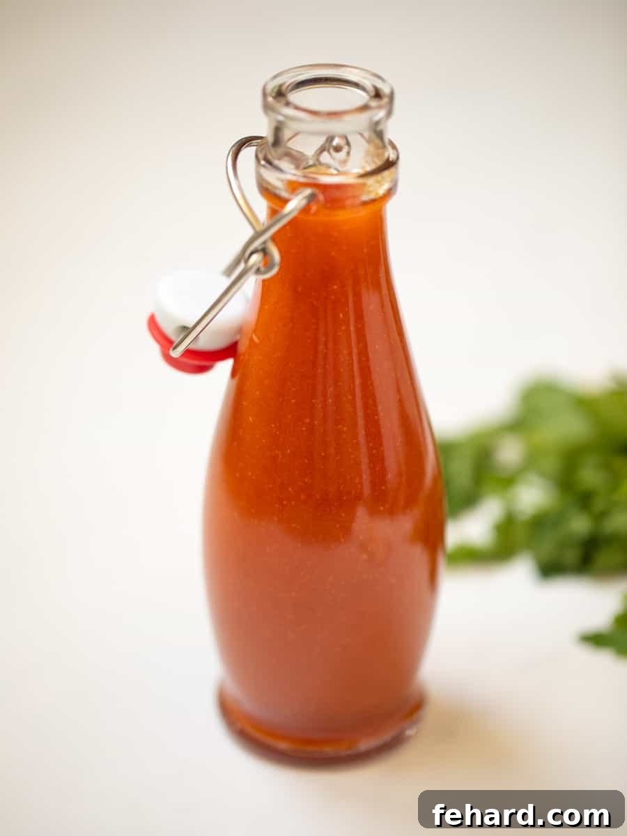 A glass jar filled with vibrant homemade buffalo sauce, garnished with fresh parsley in the background, signaling freshness and bold flavor.