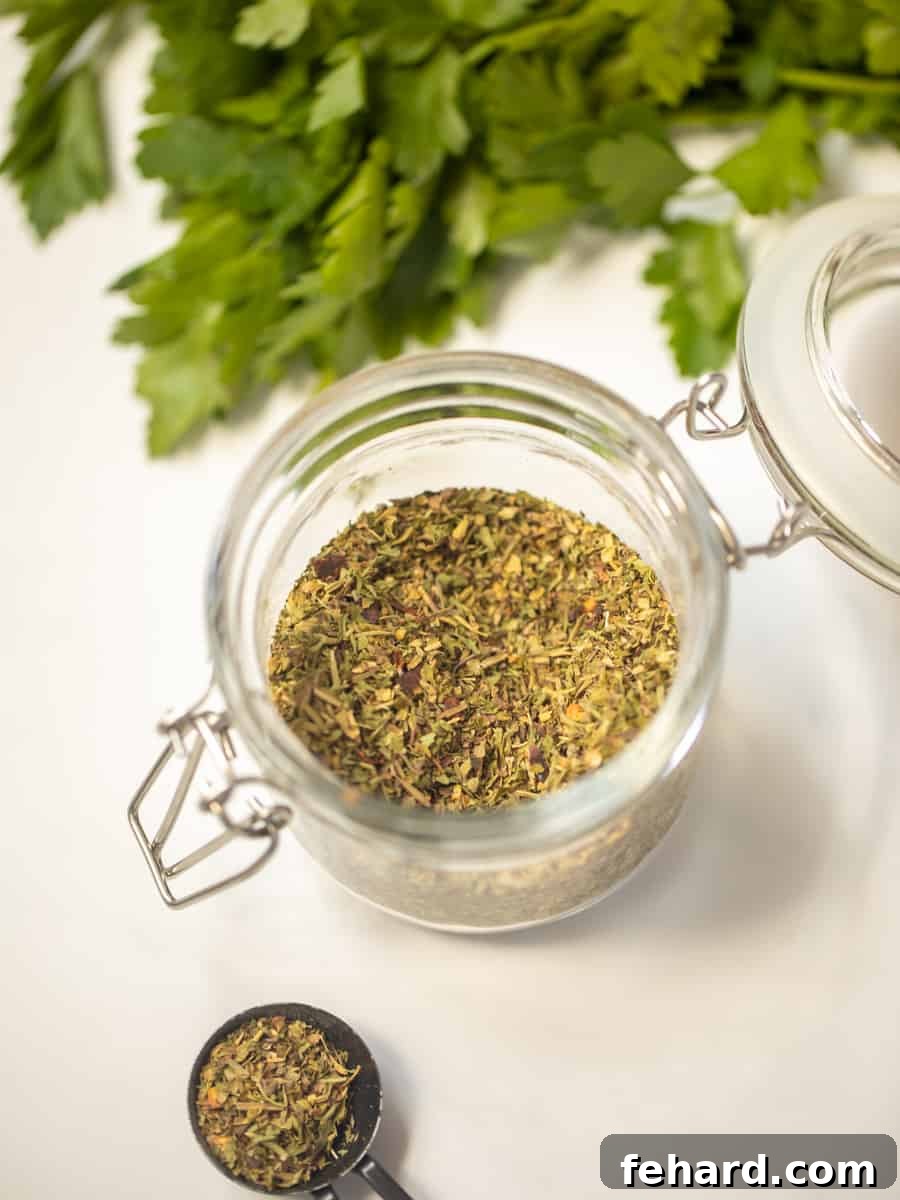 A jar of freshly made homemade Italian Seasoning sits on a kitchen counter next to a measuring spoon, ready for use.