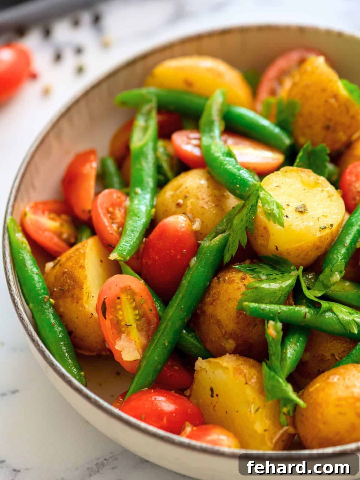 A vibrant bowl of Italian potato salad topped with fresh parsley, showcasing tender potatoes, green beans, and cherry tomatoes, all dressed in a light vinaigrette.