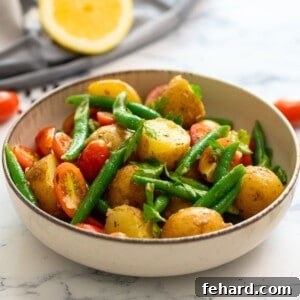 A bowl of vibrant Italian potato salad, garnished with fresh parsley, with fresh lemons and tomatoes in the background.