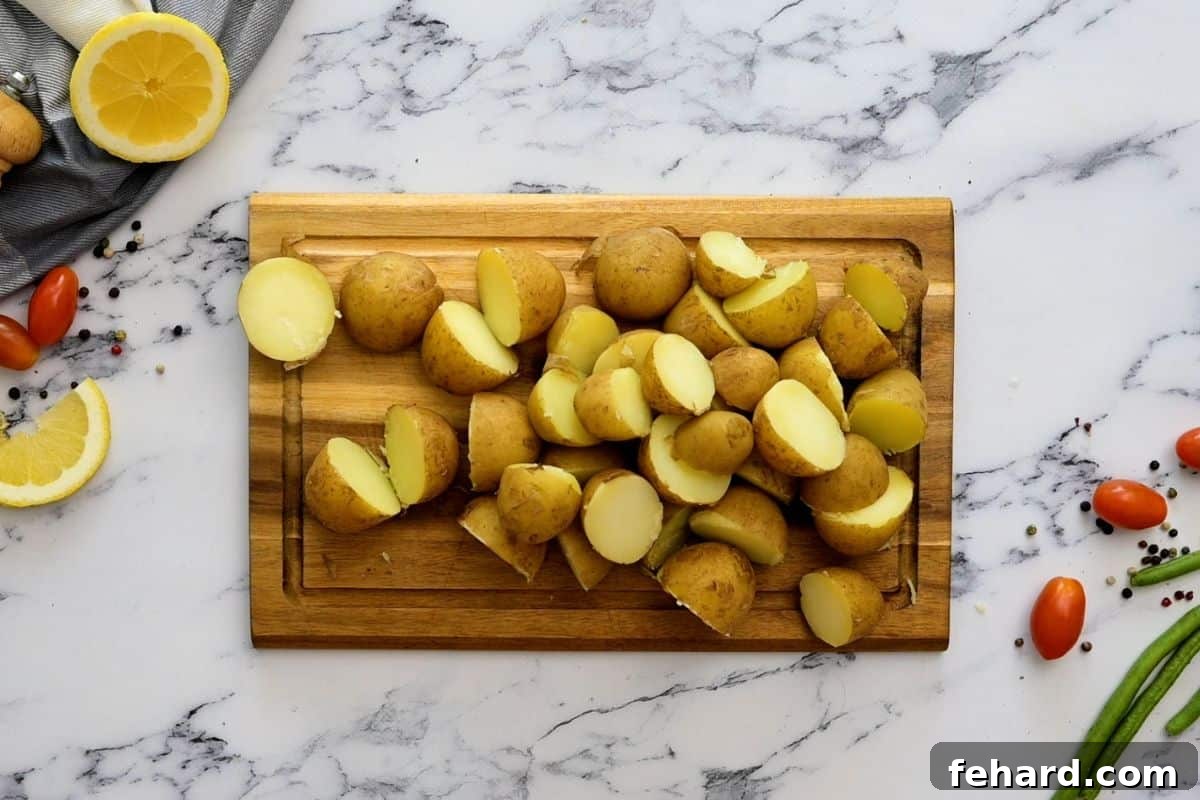 Halved baby new potatoes on a cutting board, ready for the salad after being boiled and slightly cooled.