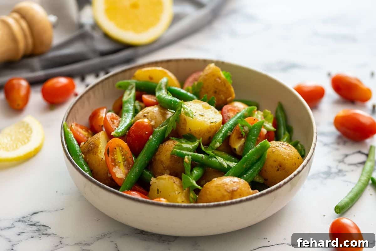 A serving bowl of Italian potato salad, garnished with fresh parsley, with fresh lemons and tomatoes blurred in the background, ready to be enjoyed.