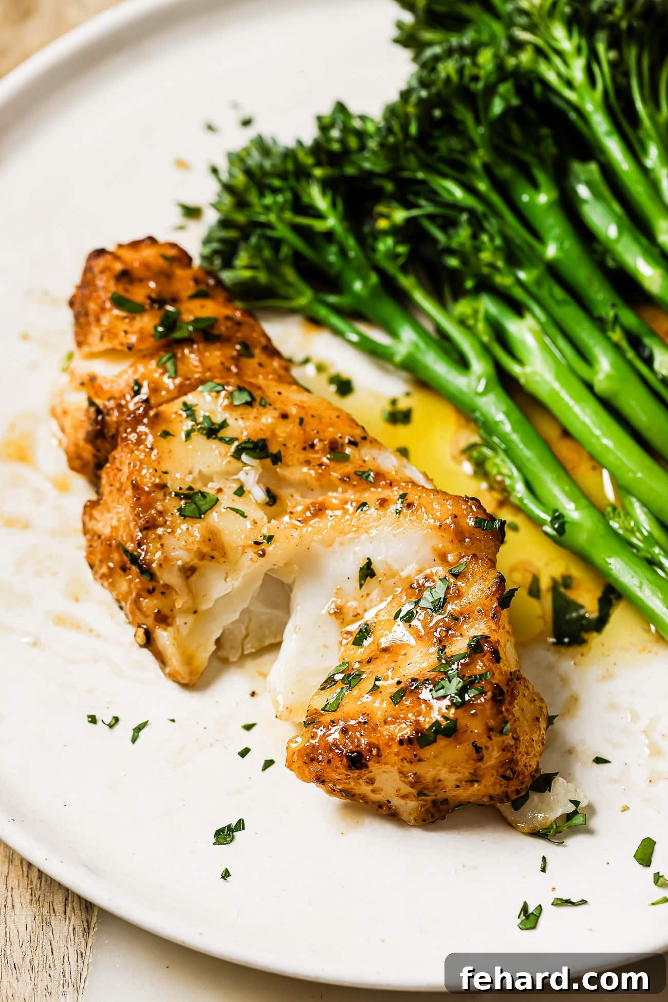 A close up of perfectly cooked air fryer cod, flaky and golden brown, garnished with fresh herbs and lemon.
