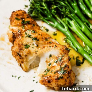 Air Fryer Cod, golden and flaky on a white plate with lemon and herbs.