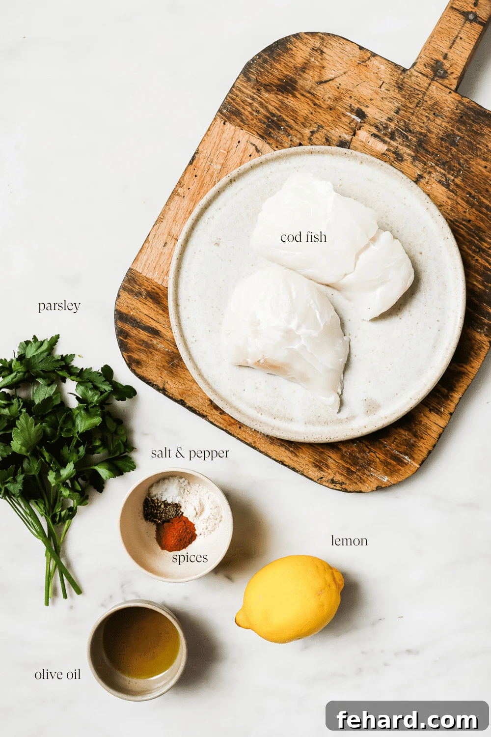 A collection of ingredients for air fryer cod, including fresh cod fillets, olive oil, paprika, garlic powder, salt, pepper, and lemon, arranged neatly against a white background.