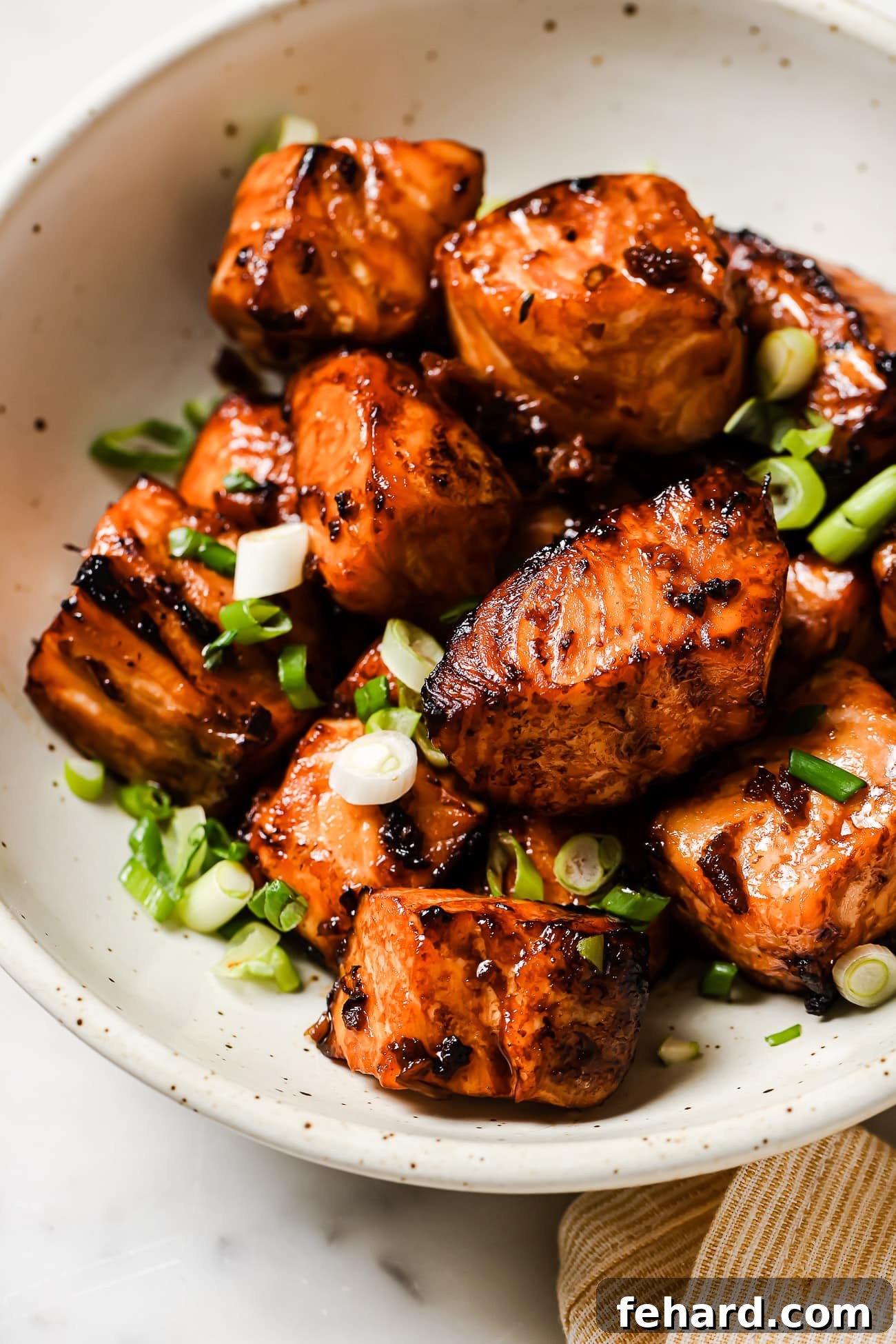 Cooked salmon bites in a white bowl, garnished with green onions and sesame seeds, ready to be served.