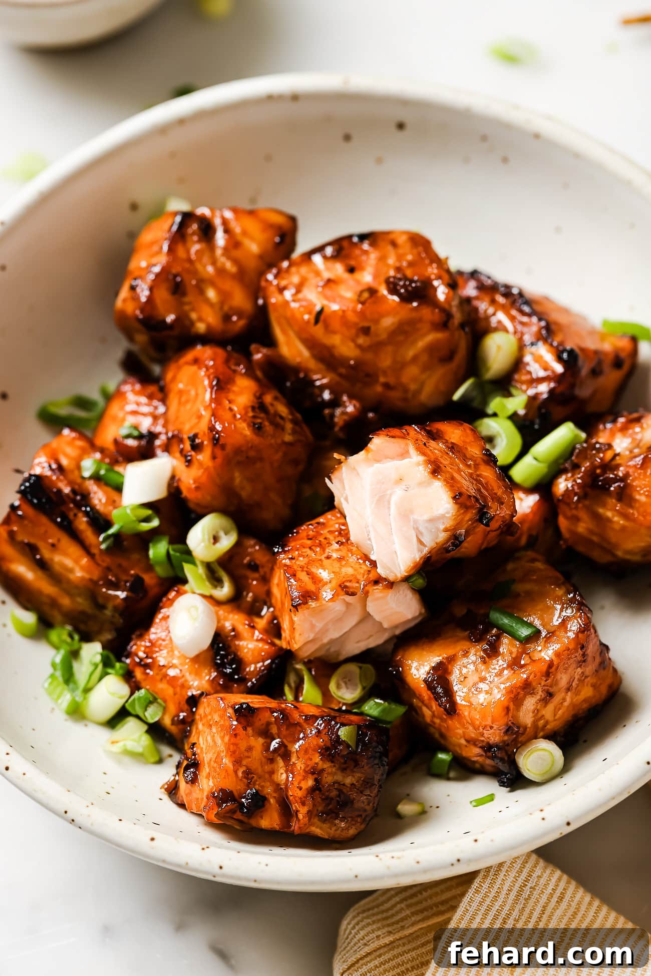 Another perspective of cooked salmon bites in a bowl, garnished with fresh green onions, ready for serving.