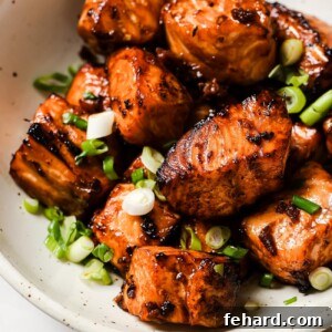 Air fryer salmon bites on a plate with rice and broccoli, garnished with green onions and sesame seeds.