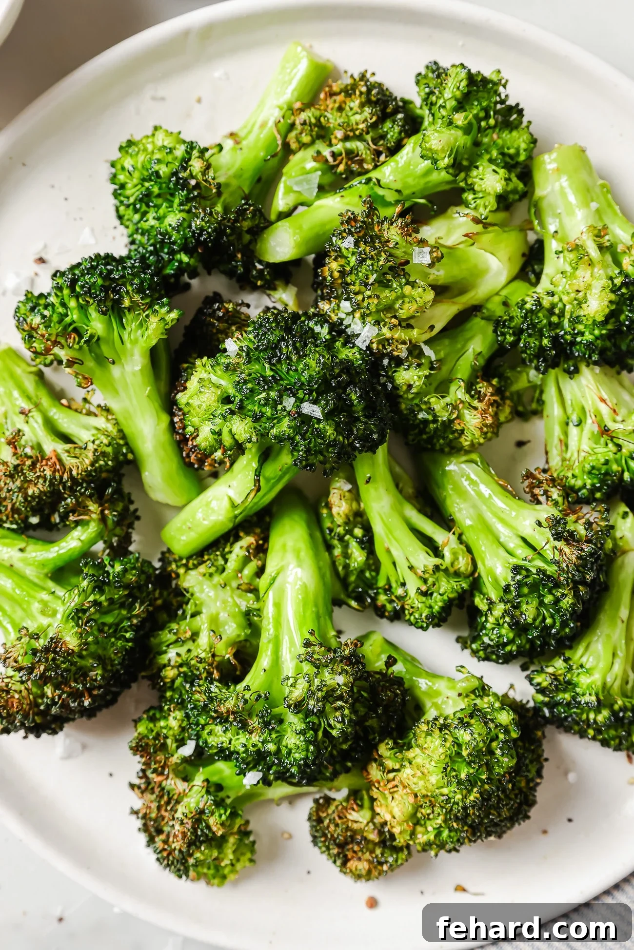 Quick & Crispy Air Fryer Broccoli 5 Air fryer broccoli on a white plate, garnished with lemon wedges, ready to serve.