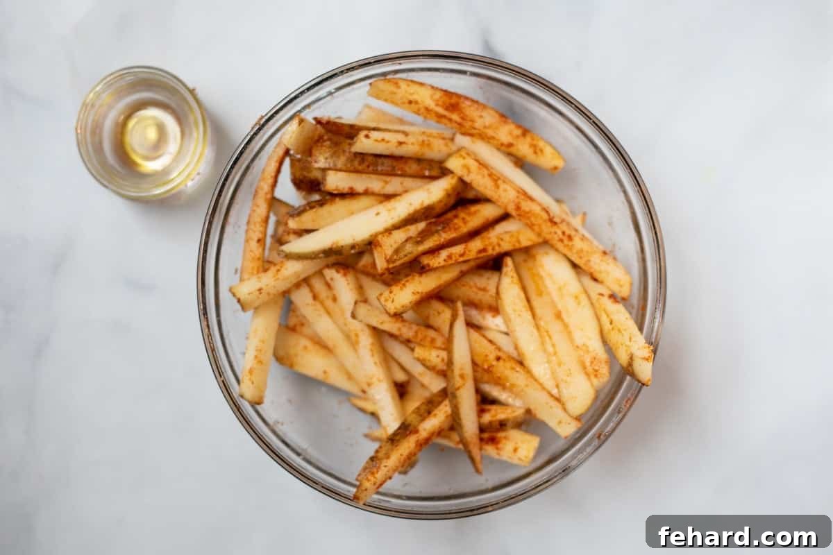 A large mixing bowl filled with thin strips of potatoes, generously seasoned with vibrant paprika, aromatic garlic powder, and coarse kosher salt, ready for air frying.