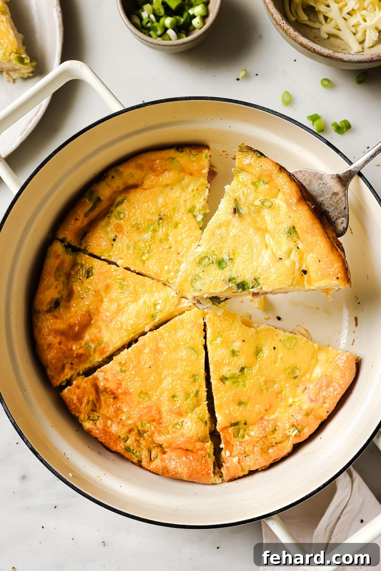 Crustless ham and cheese quiche cut into slices in a pie dish, showcasing its golden-brown top and fluffy interior.