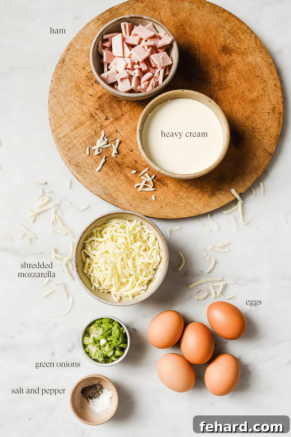 Pre-measured ingredients for crustless quiche, including eggs, heavy cream, diced ham, and shredded cheese, arranged in small bowls on a wooden cutting board.