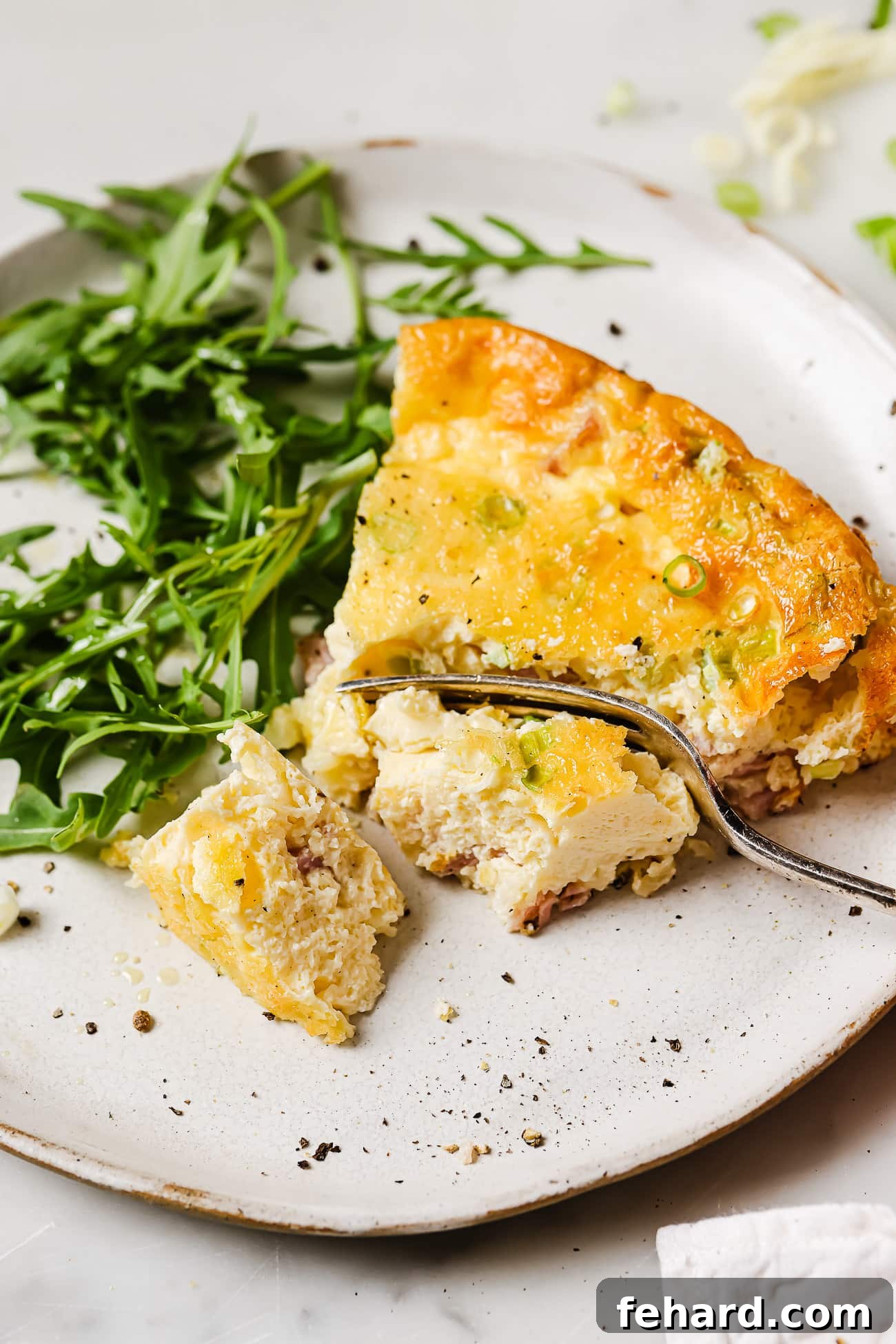 A perfectly portioned slice of crustless ham and cheese quiche artfully plated alongside a fresh arugula salad, ready to be enjoyed.