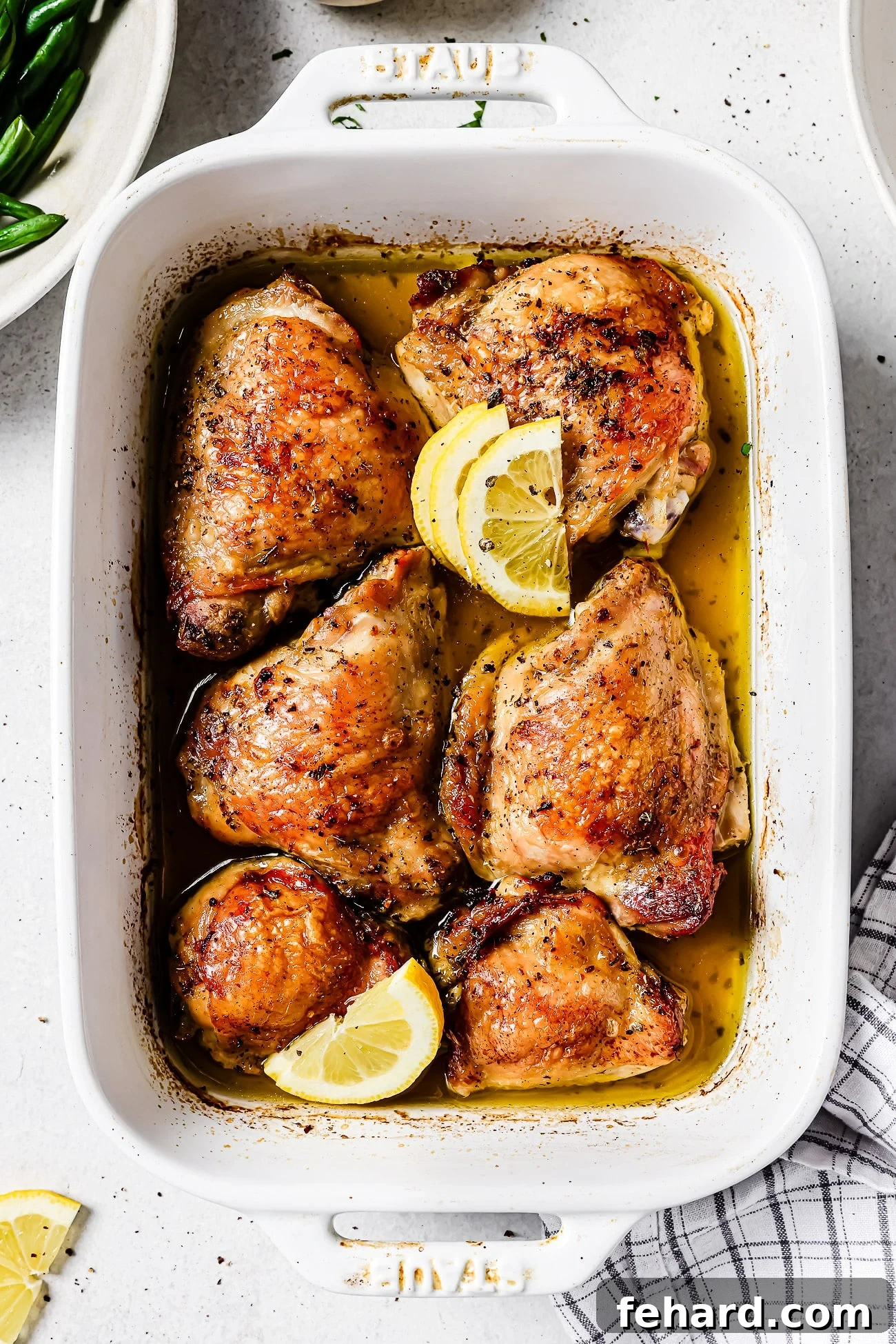 Zesty Lemon Chicken Thighs 6 Beautifully roasted lemon chicken thighs glistening with pan juices, arranged in a baking dish and elegantly garnished with fresh lemon wedges, showcasing a perfect golden crust.