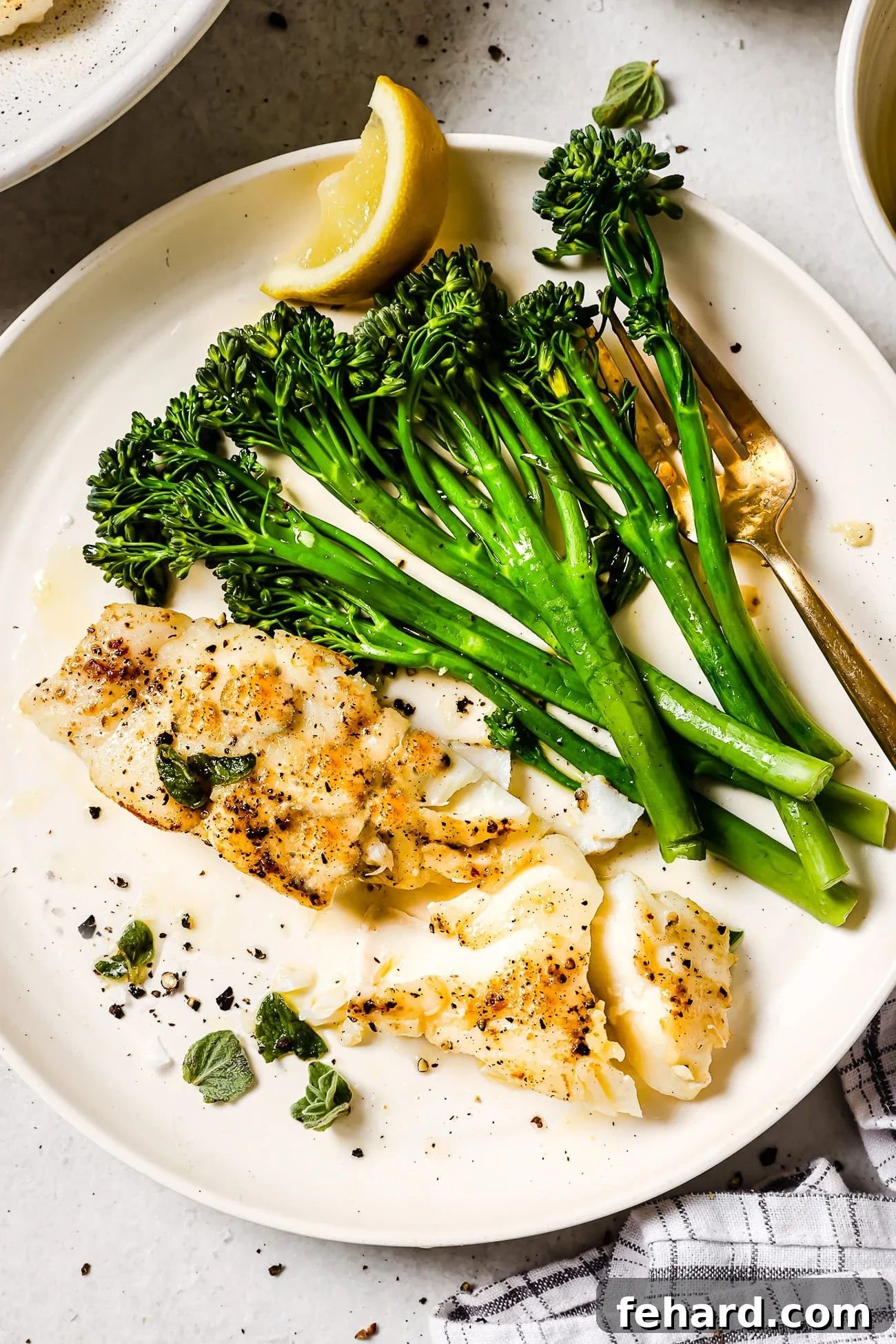 Pan-Seared Garlic Butter Haddock 8 Garlic butter haddock on a white plate with broccolini and a lemon wedge.