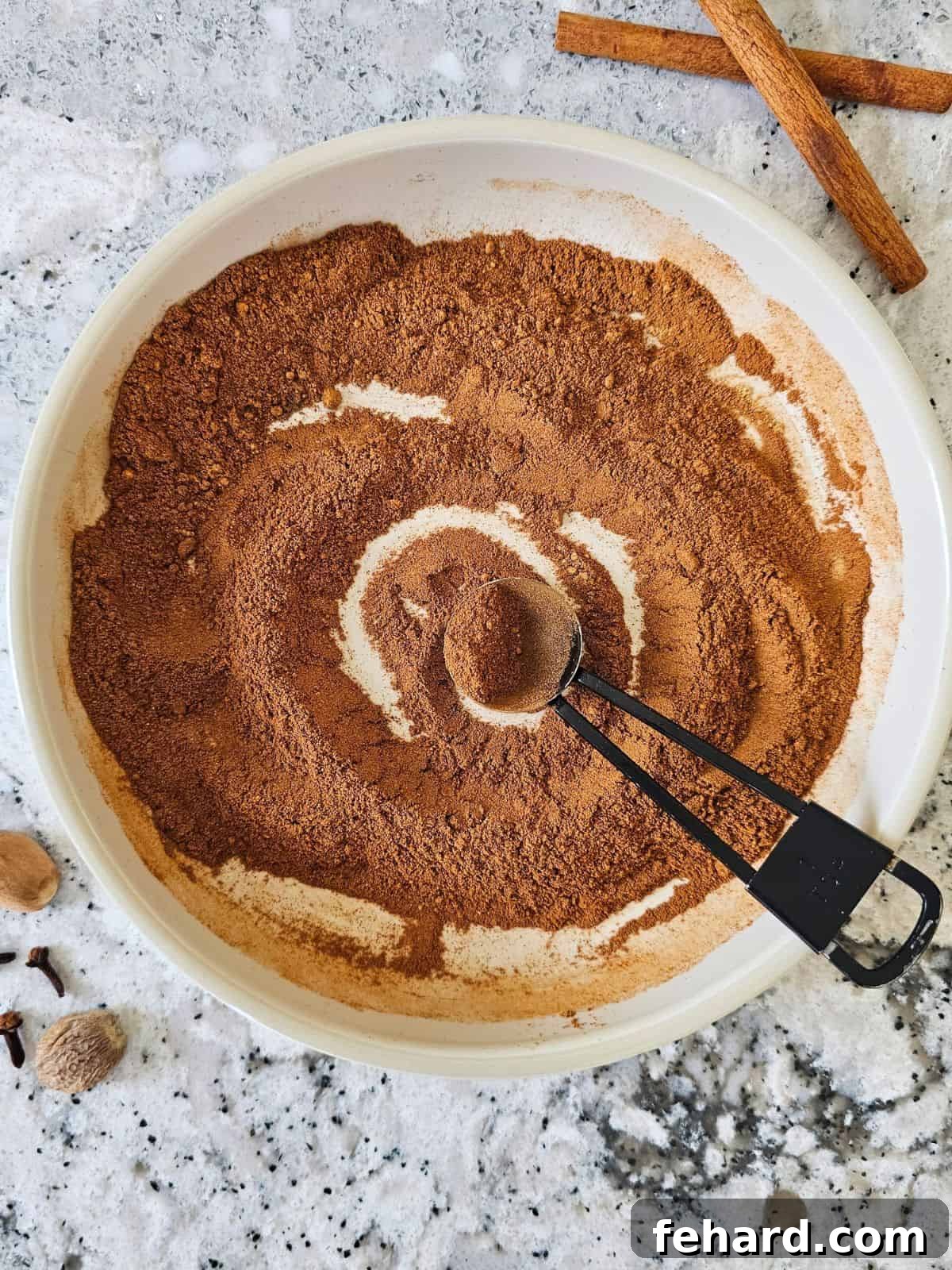 Ingredients for pumpkin pie spice blend whisked together in a small bowl, showcasing the rich colors of cinnamon, nutmeg, ginger, cloves, and allspice.