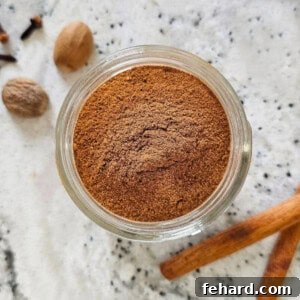 Small spice jar with homemade pumpkin pie spice blend next to cinnamon sticks and whole nutmeg.
