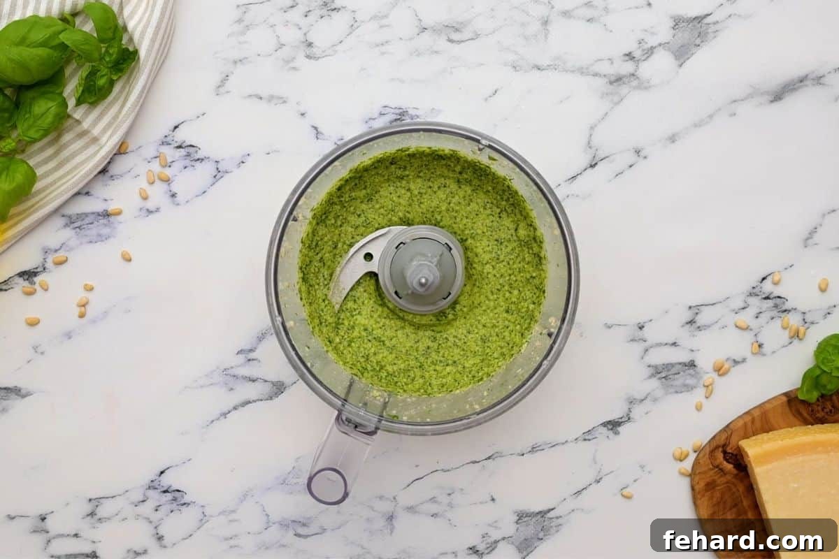 Homemade basil pesto being prepared in a food processor, vibrant green and smooth.