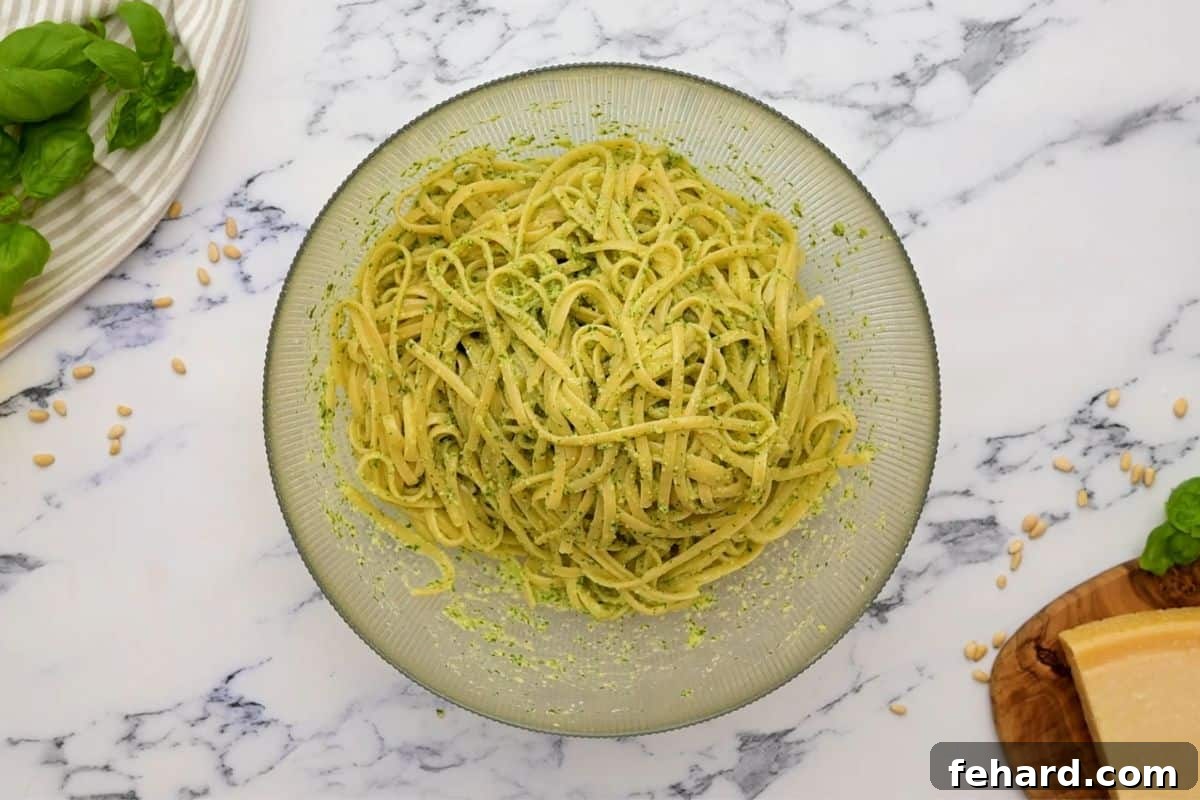 Cooked linguine noodles being tossed with vibrant homemade basil pesto in a large mixing bowl.