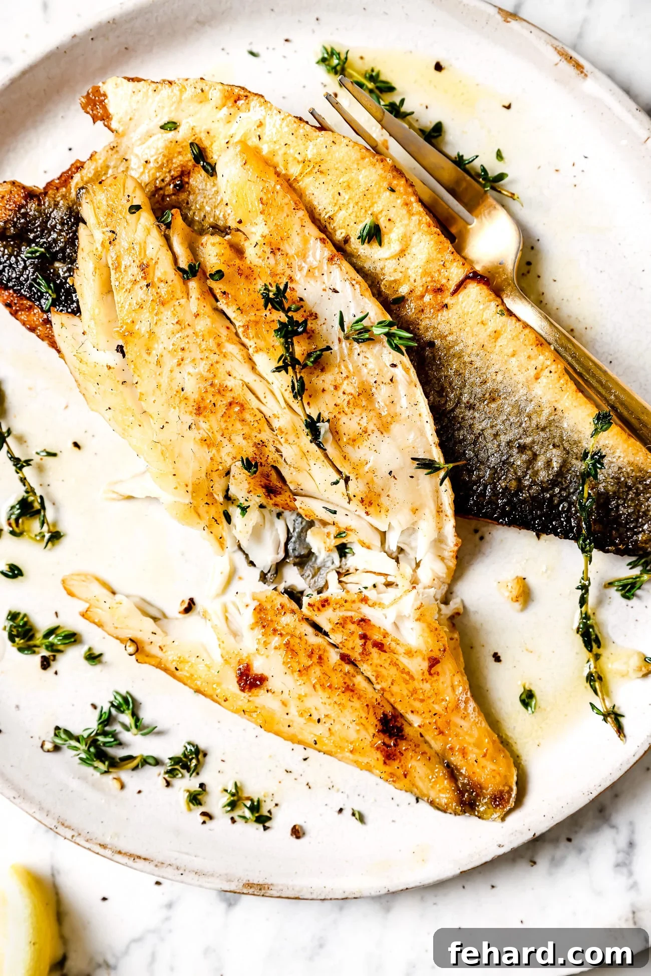 Succulent Garlic Butter Sea Bass Recipe 2 Sea Bass garnished with fresh thyme, butter and garlic on a white plate, served with lemon wedges.