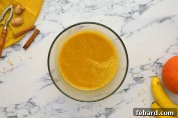 A bowl showcasing pumpkin puree, eggs, mashed banana, and maple syrup, all perfectly blended together.