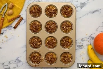 Twelve pumpkin banana muffin cups, each generously topped with streusel, ready for baking.