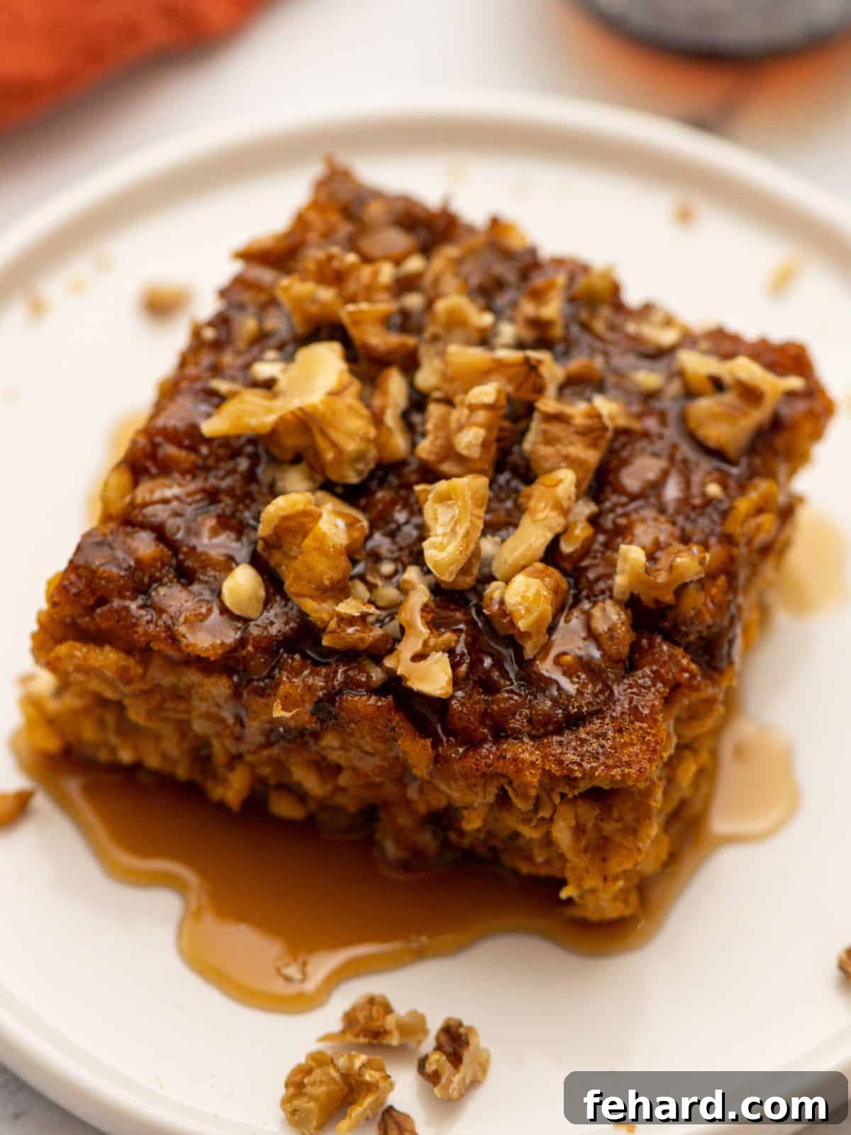 A perfectly portioned slice of baked pumpkin oatmeal rests on a plate, elegantly drizzled with golden maple syrup and garnished with a sprinkle of finely chopped walnuts. This inviting image captures the cozy, hearty nature of a healthy fall breakfast, brimming with warming spices, rich pumpkin, and wholesome oats.