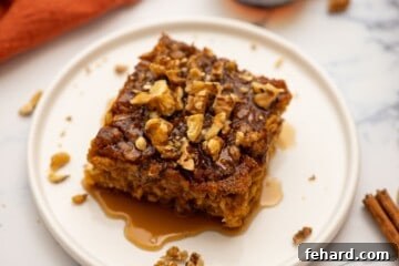 Slice of baked pumpkin oatmeal on plate topped with maple syrup and nuts.