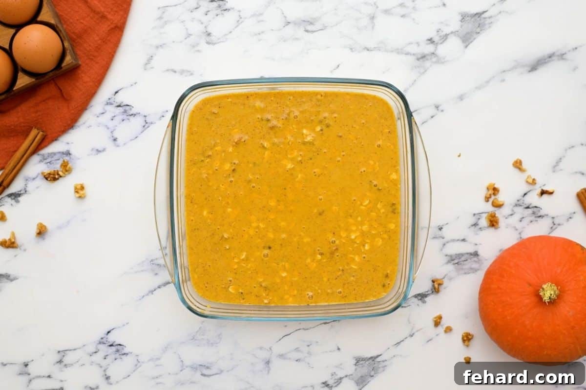 The pumpkin oatmeal mixture, with its vibrant orange hue and visible oats, is carefully poured into a clear 8x8 inch glass baking dish, ready for resting and baking. This image highlights the simplicity of the preparation process.