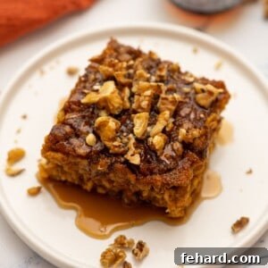 Slice of baked pumpkin oatmeal on plate topped with maple syrup and chopped nuts.