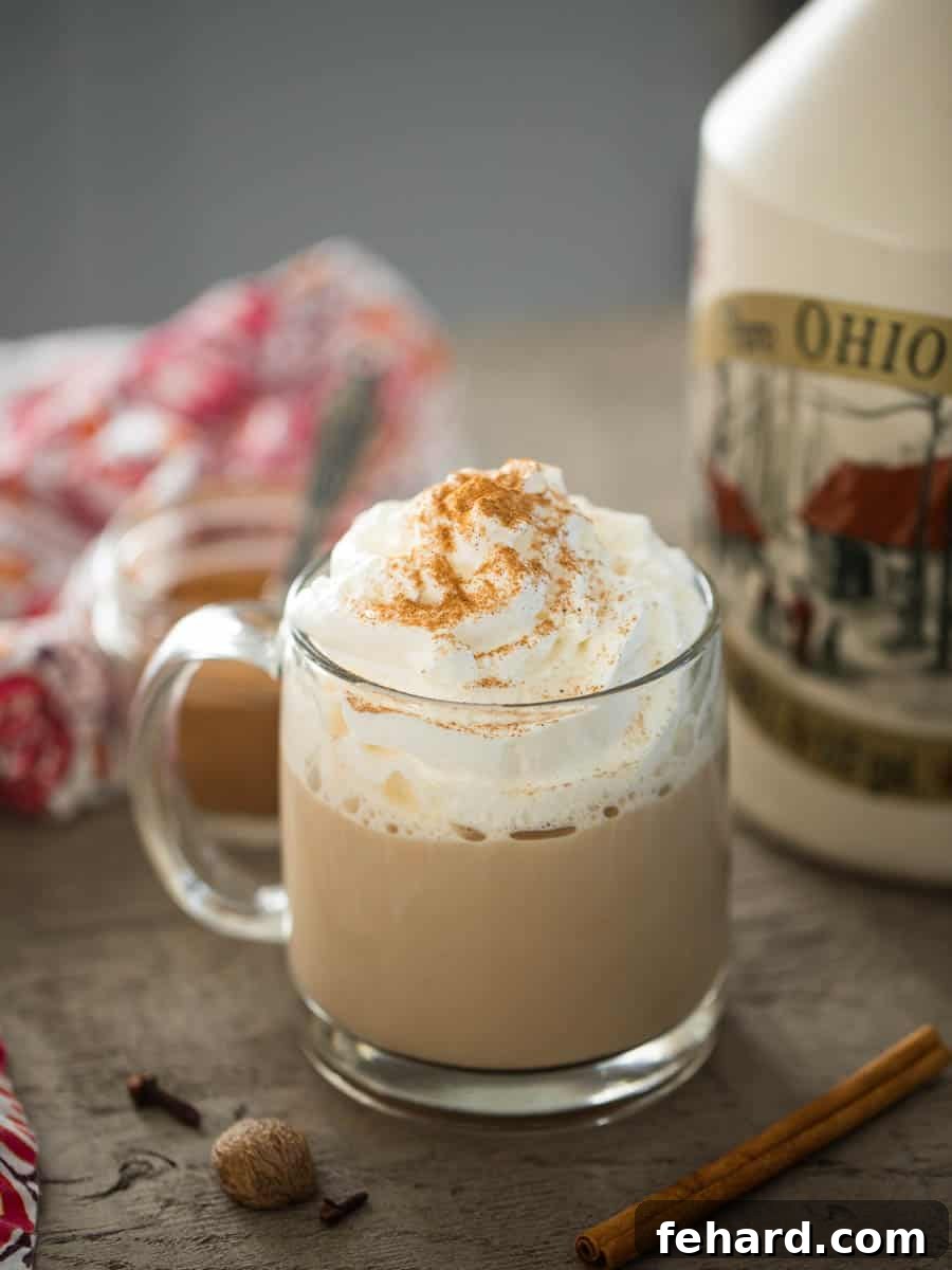 Homemade Pumpkin Spice Latte in a clear glass mug, with maple syrup and cinnamon sticks elegantly arranged in the background, exuding cozy fall vibes.