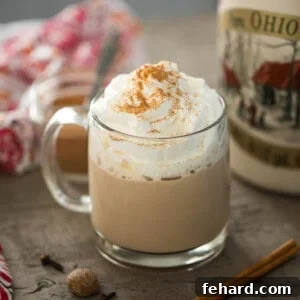 Pumpkin spice latte in clear glass much with maple syrup and cinnamon sticks in background.