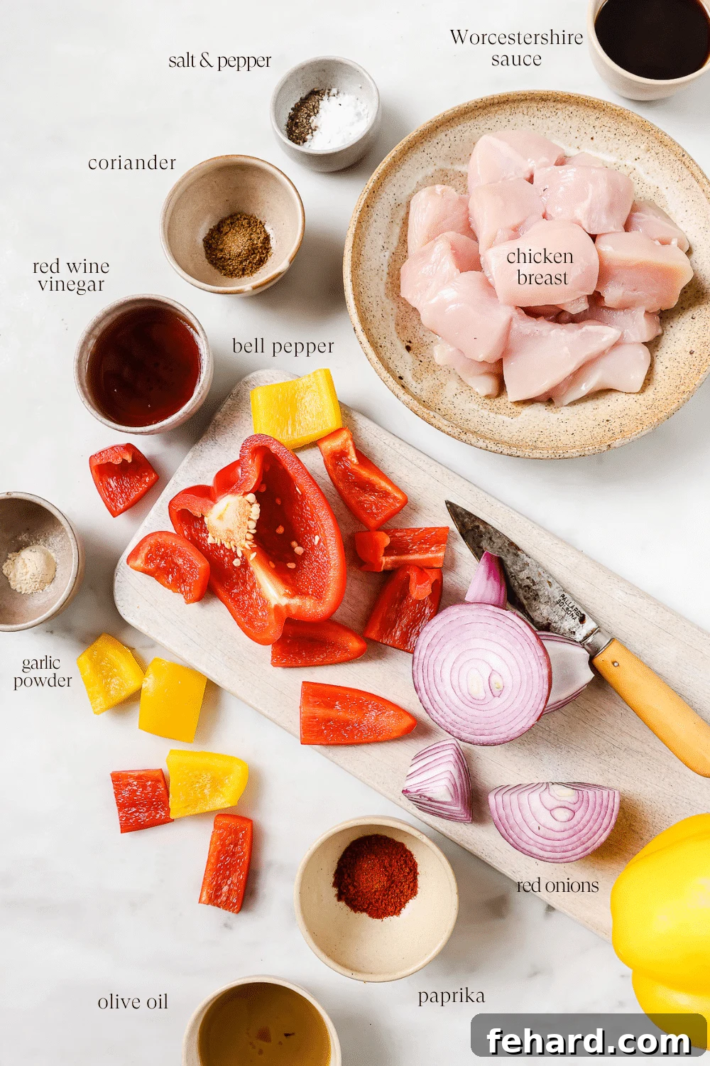 Prepped ingredients for chicken kabobs, including diced chicken, bell peppers, and marinade in a bowl, arranged neatly on a white countertop.