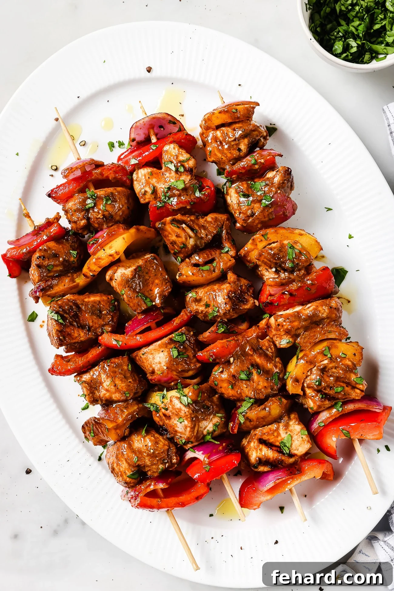 An overhead view of four beautifully arranged chicken kabobs on a white serving plate, garnished and ready to be served.
