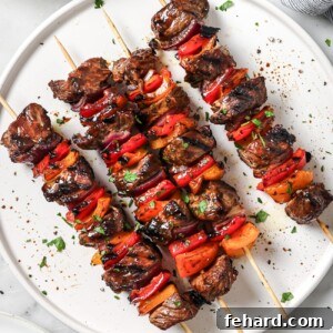 A close-up image of two beef kabobs on a white plate, showcasing the tender steak and colorful vegetables, with a fresh lemon wedge.