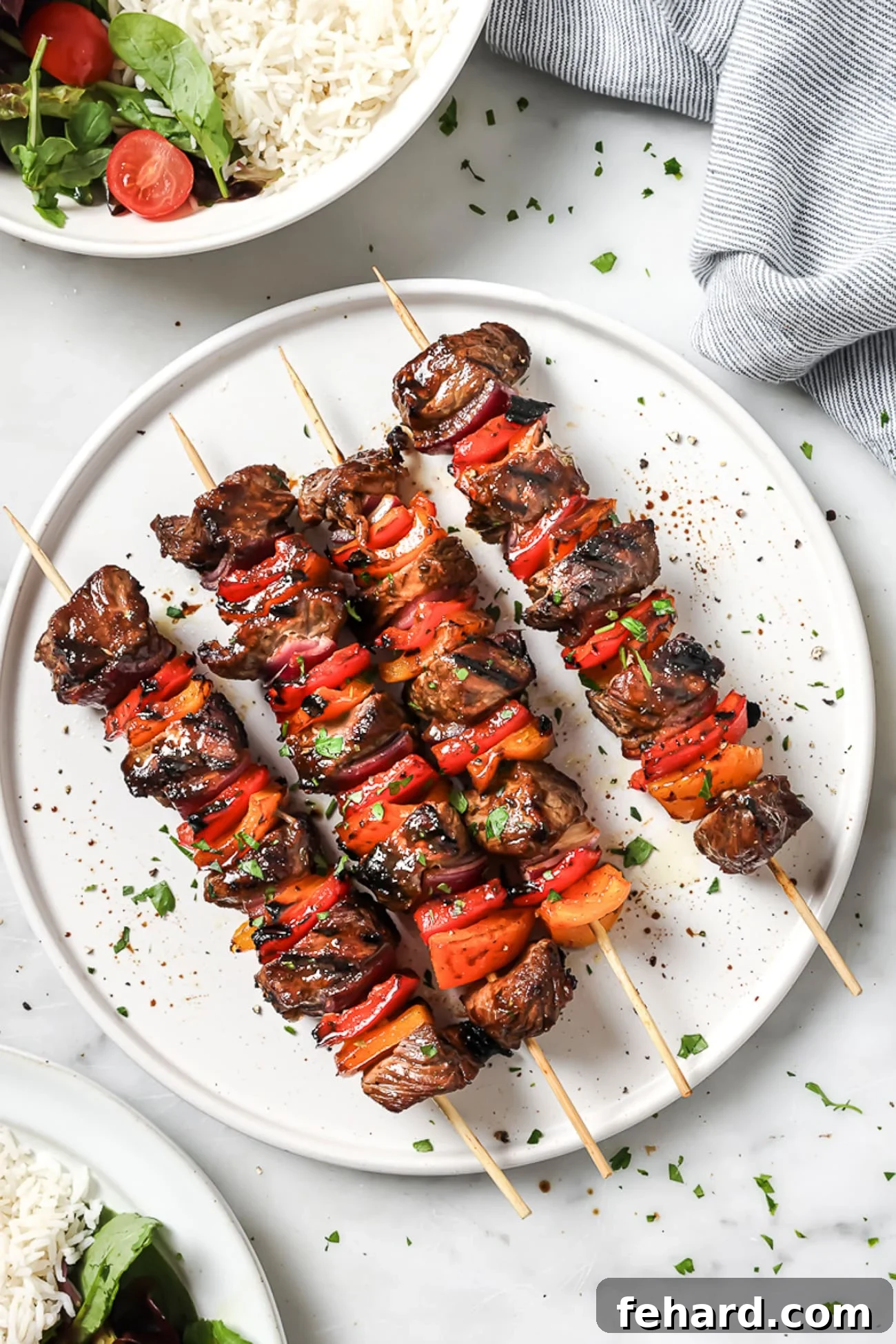 An overhead view of four perfectly grilled beef kebabs arranged on a pristine white serving plate.