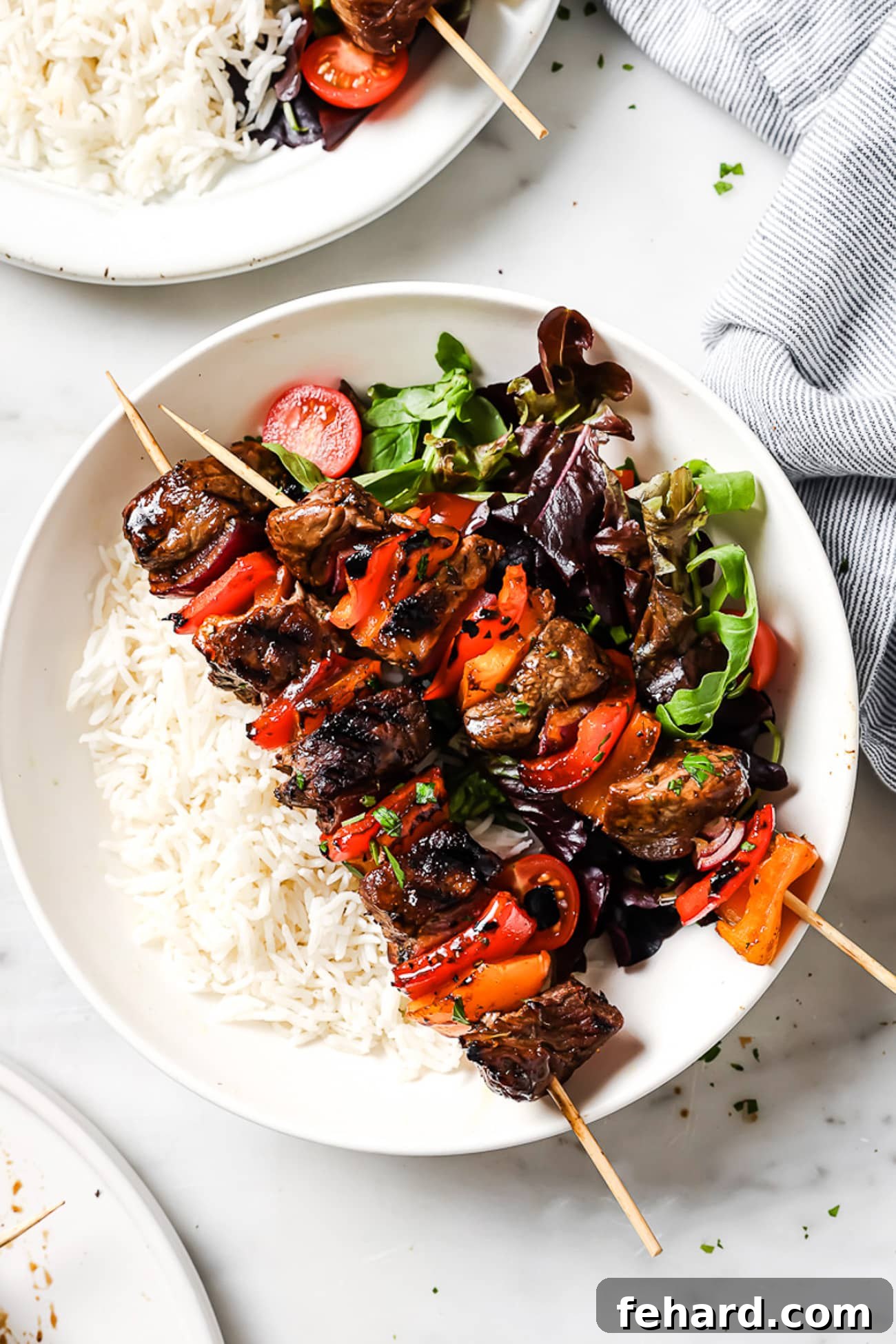 Two beef kebabs elegantly presented on a bed of fluffy white rice, accompanied by a vibrant green salad.
