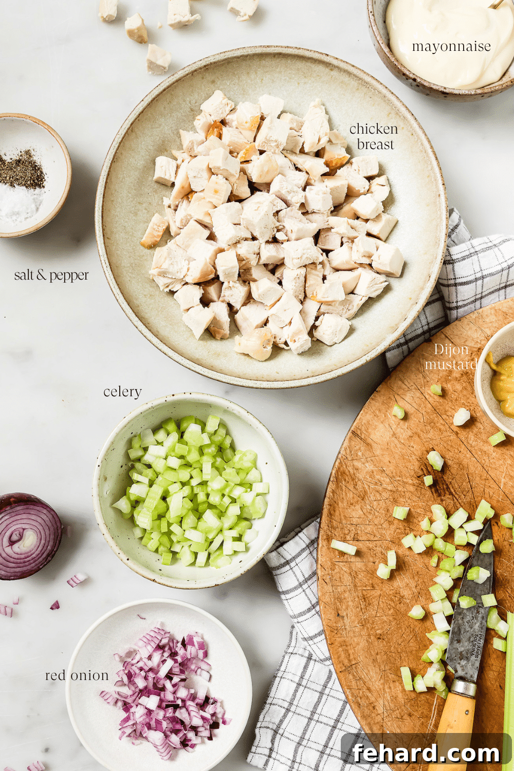 Signature Chicken Salad 3 Small bowls of prepped ingredients laid out neatly on a white countertop, ready for mixing.