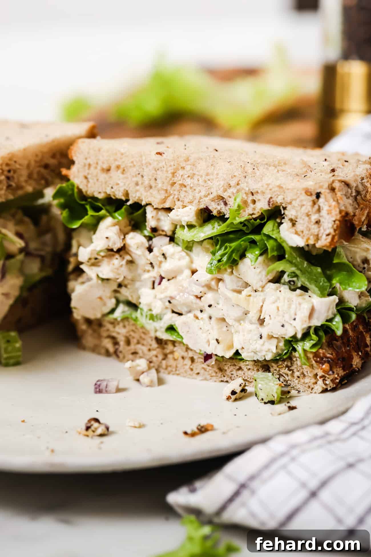 Signature Chicken Salad 6 A close-up shot of half a chicken salad sandwich on a pristine white plate, garnished with fresh lettuce.