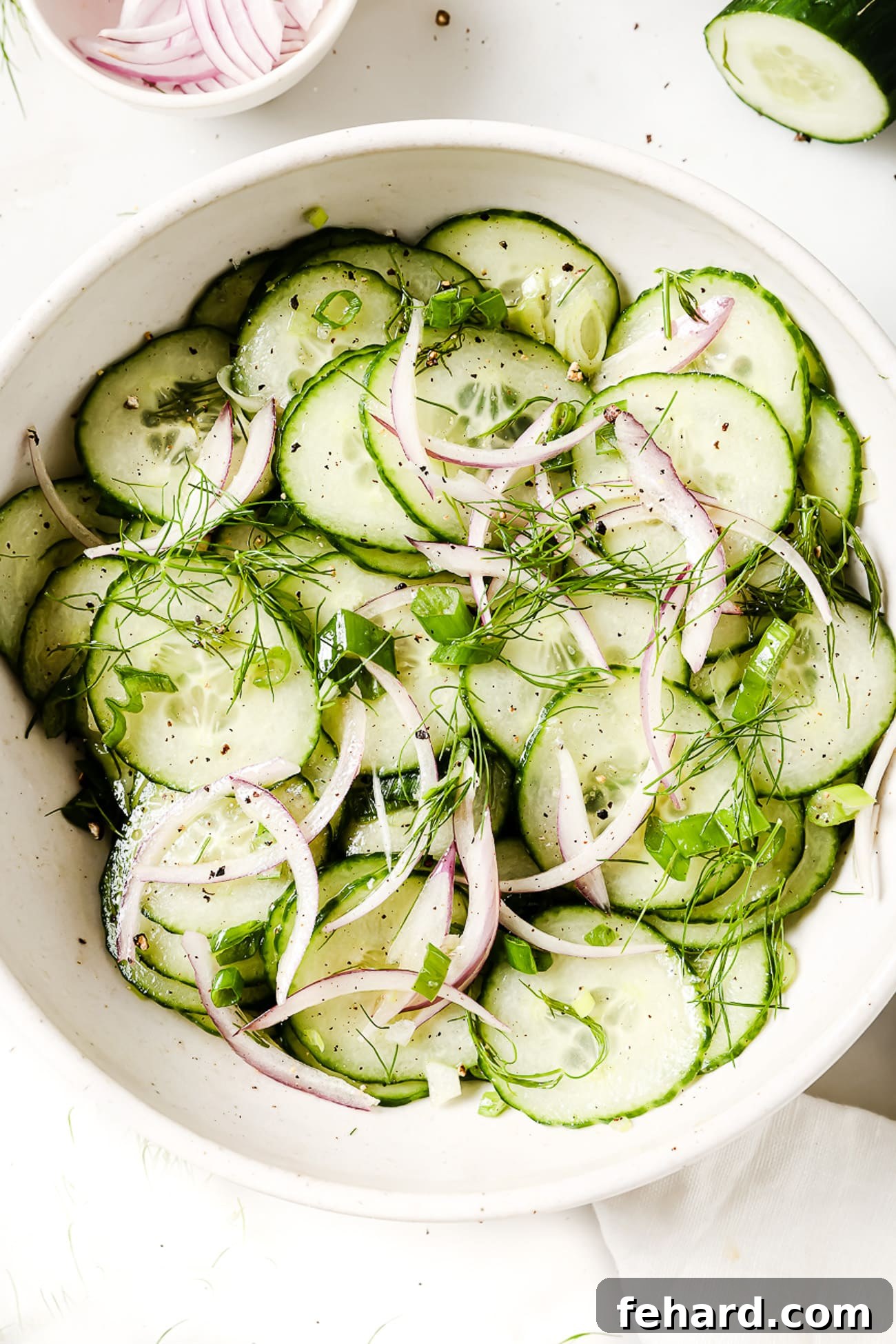 An overhead view of a large white bowl filled with a fresh, vibrant cucumber salad, ready to be served.