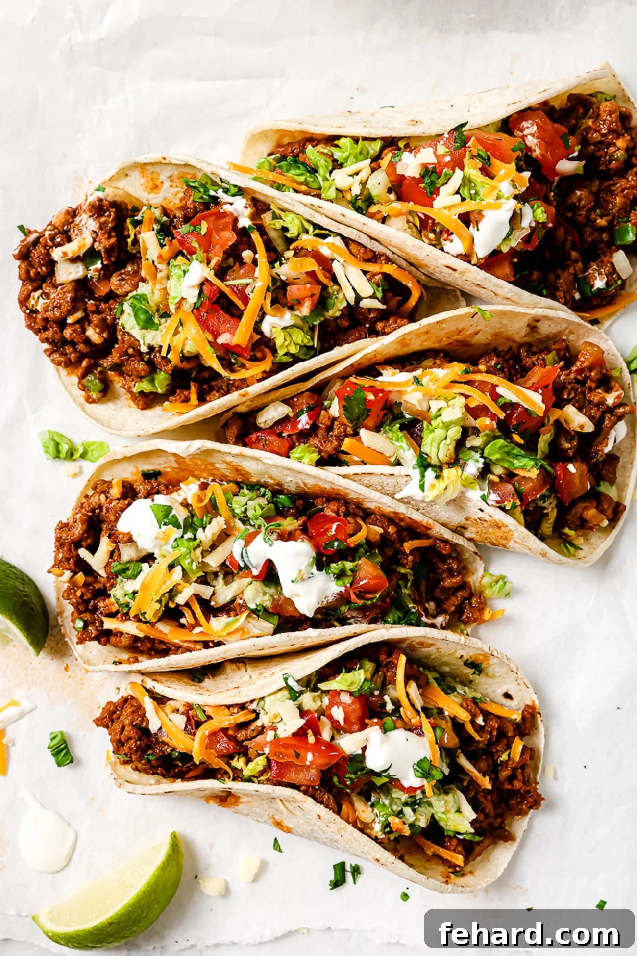 Five ground beef tacos arranged on parchment paper, showcasing their delicious filling and fresh toppings.