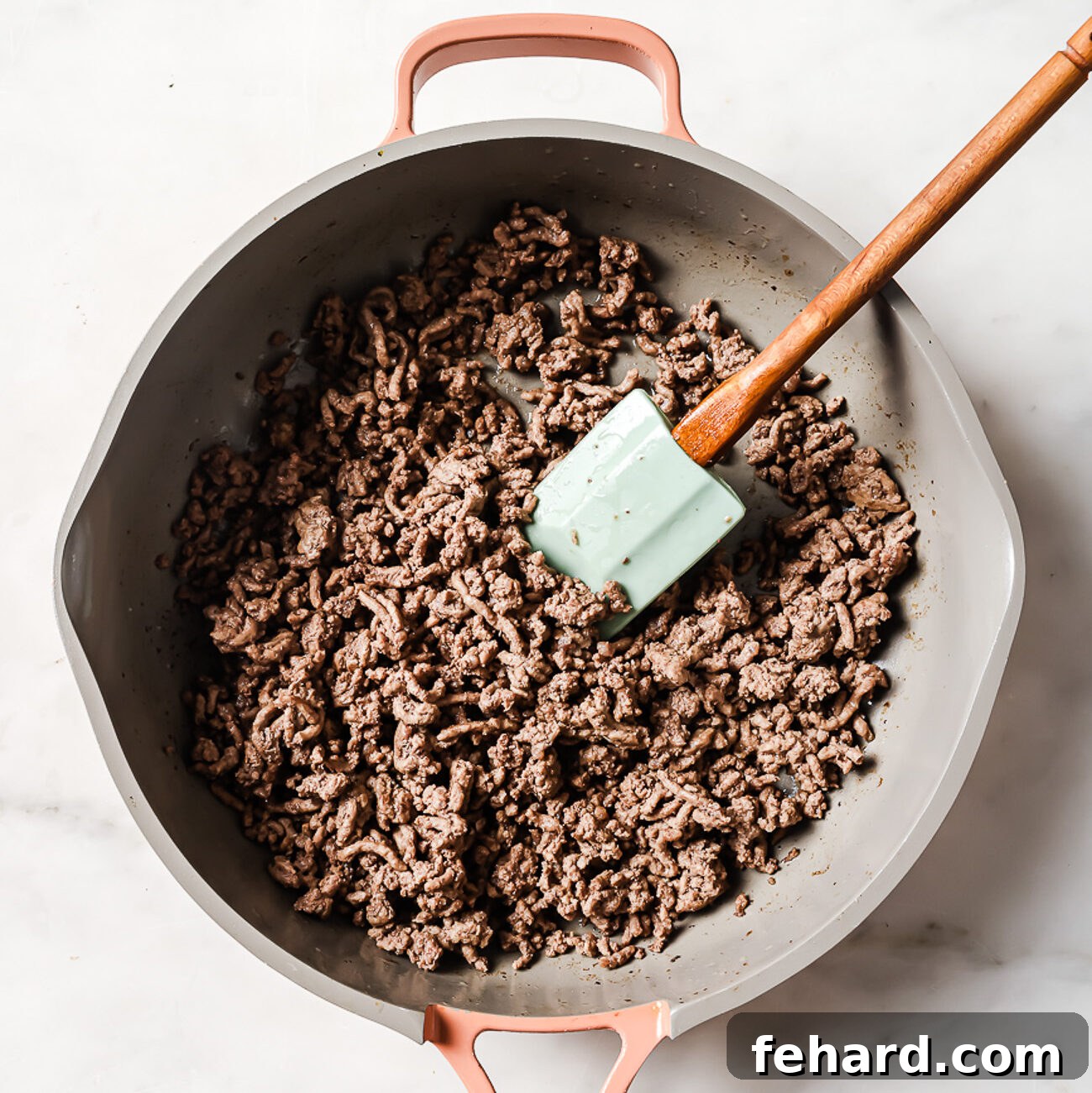 Ground beef cooking in a skillet, broken into small pieces and browning evenly.