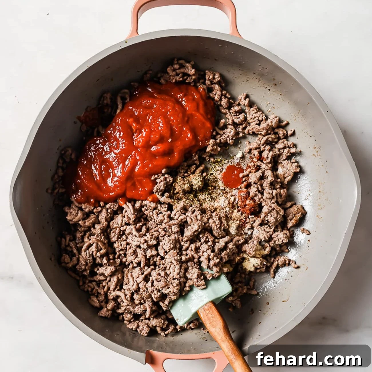 Ground beef, tomato sauce, and seasonings being stirred together in a skillet, creating a rich and fragrant mixture.